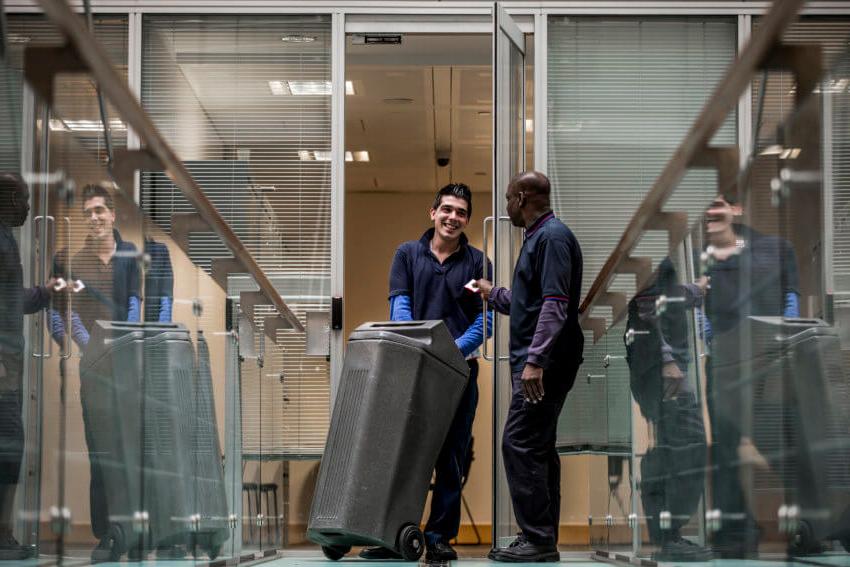 Two Mitie 浪费 workers taking a grey bin out